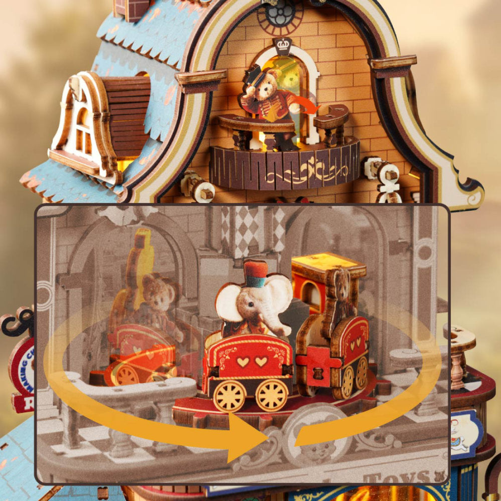 A decorative wooden toy train house shown with an inset diagram explaining movement. The top half shows the assembled toy with a small mouse figure in a train and a balcony scene above.