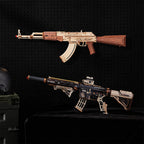 Two miniature replica-style rifle models displayed against a black pegboard background, with one mounted on the wall and one placed on a black surface below. A helmet and storage case are partially visible at the left edge.