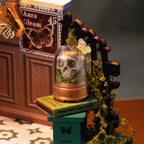 A miniature decorative display featuring a glass dome with a small skull and butterfly, placed on a green pedestal next to a dark wooden arch with yellow-green moss, in a styled tabletop scene.
