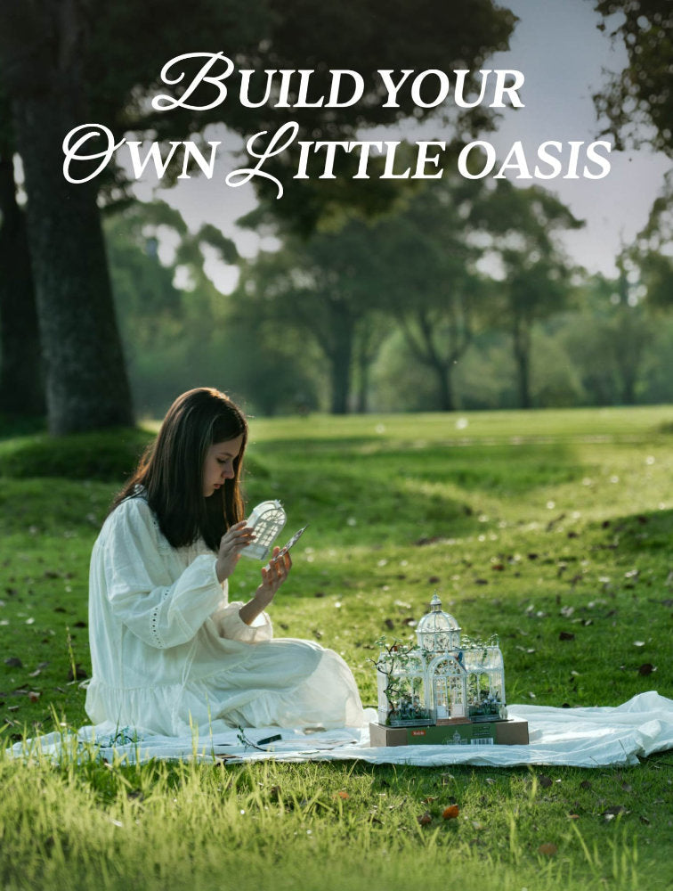 A woman in a white dress sits on a blanket in a grassy park, arranging small glass terrariums. Large white text at the top reads 'Build your own little oasis'.