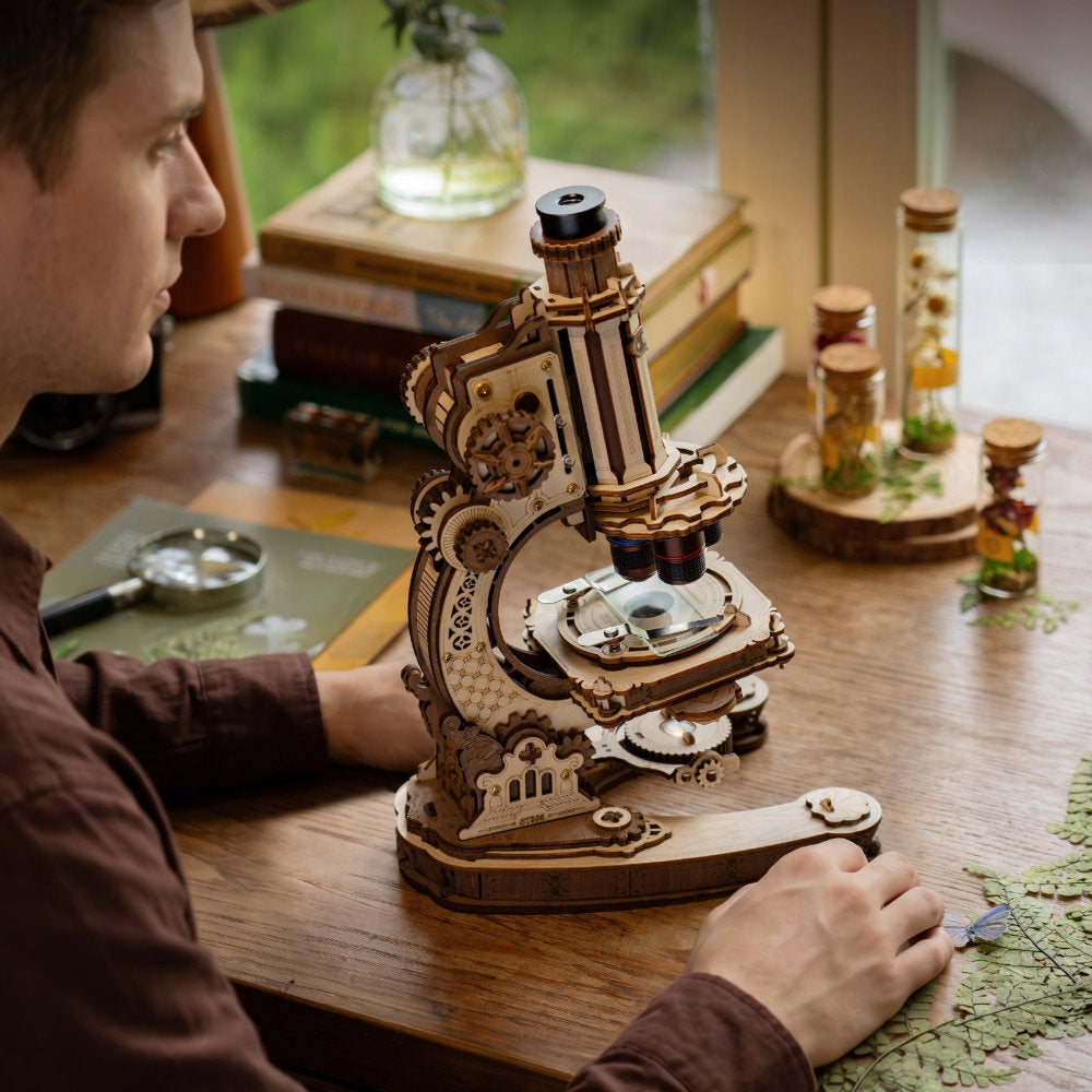 Man using a wooden microscope on a table with books and bottles in the background