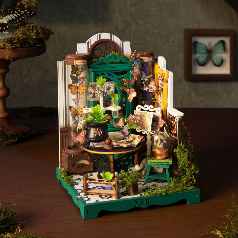 A highly detailed miniature diorama set up on a dark wooden table, featuring a gothic-style room with a green door, glass case displays, a skull on a bookshelf, and various decorative insects and plants.