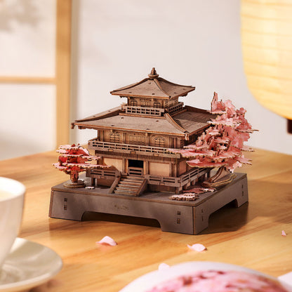 Wooden model of a traditional Japanese temple with cherry blossom trees on a wooden table.