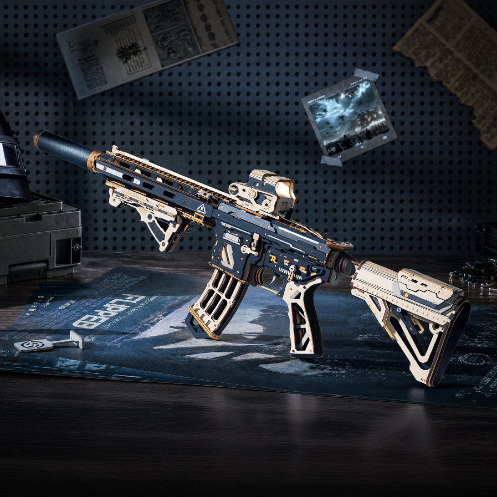 A highly detailed miniature model of a tactical rifle, styled on a desk with a desk mat and surrounded by sci-fi themed props against a dark pegboard wall.