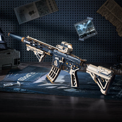 A highly detailed miniature model of a tactical rifle, styled on a desk with a desk mat and surrounded by sci-fi themed props against a dark pegboard wall.