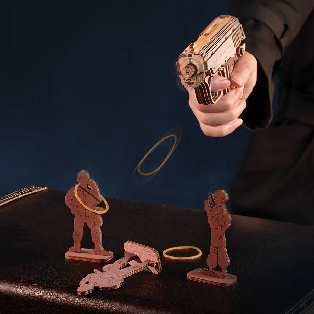 Hand holding a toy gun over a table with toy figures and props on a dark background