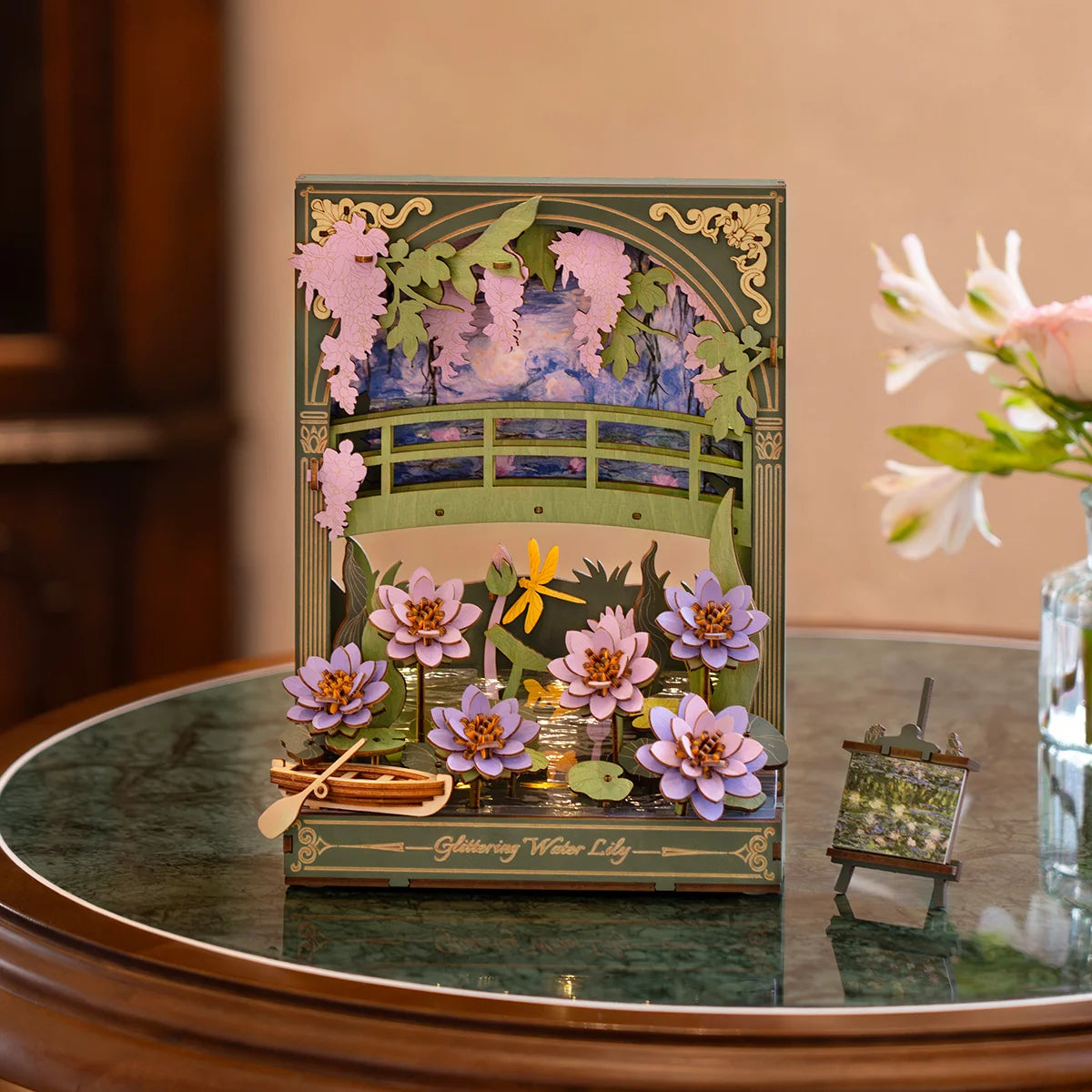 Decorative card with a pond scene featuring flowers and a bridge on a wooden table.
