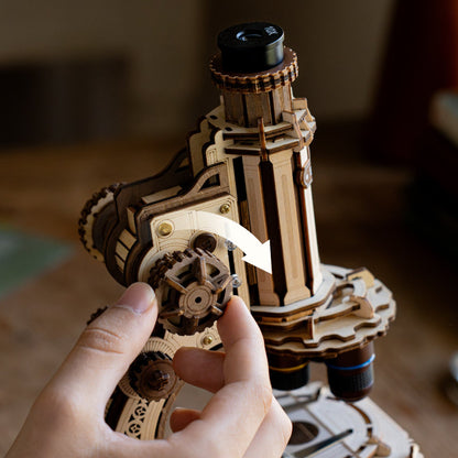 Wooden mechanical model of a lighthouse with gears, held by a hand.