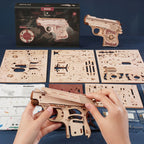 Wooden gun model kit with hands assembling it, packaging in the background