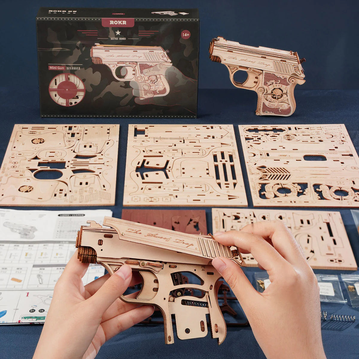 Wooden gun model kit with hands assembling it, packaging in the background