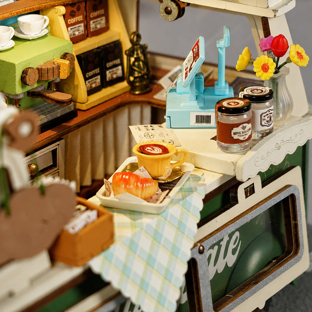 Toy coffee shop set with miniature coffee machine, cups, and flowers.