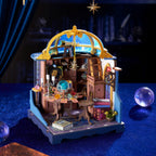 A miniature fantasy observatory and library dollhouse set on a dark blue textured surface, featuring a blue and gold dome, wooden interior shelves, a telescope, books, and small decorative props.
