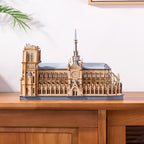 Wooden model of a cathedral on a wooden surface with a white wall and plant in the background