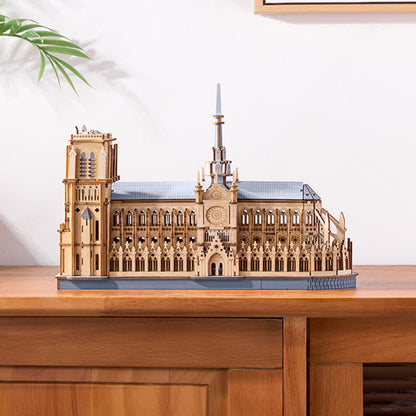 Wooden model of a cathedral on a wooden surface with a white wall and plant in the background