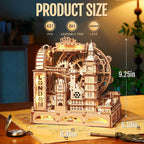 Wooden mechanical model of a London-themed building with size measurements on a table.