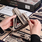 A person's hands are assembling a wooden 3D model of a firearm, holding a layered wooden piece over a sheet of corresponding laser-cut wood pieces. The product box labeled 'JUSTICE GUARD MA14 CARRINE' is visible in the background along with other assembly sheets.