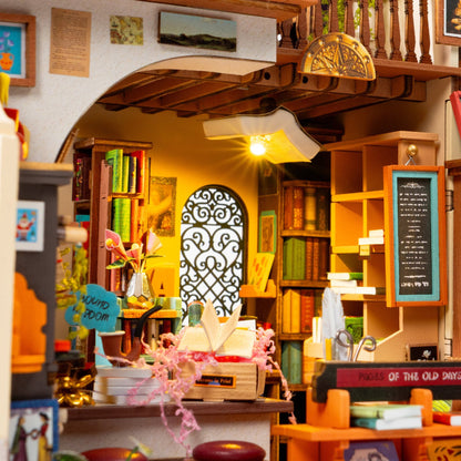 A miniature bookshop dollhouse interior with tiny bookshelves, a chalkboard, hanging lanterns, and warm yellow lighting, photographed as a product scene rather than a real environment.