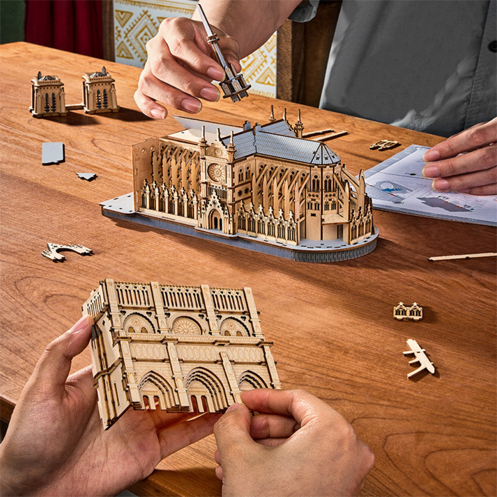 People assembling a wooden model of a cathedral on a wooden table.