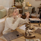 Woman working on a model kit at a table with various components and tools.