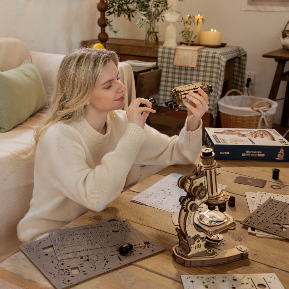 Woman working on a model kit at a table with various components and tools.
