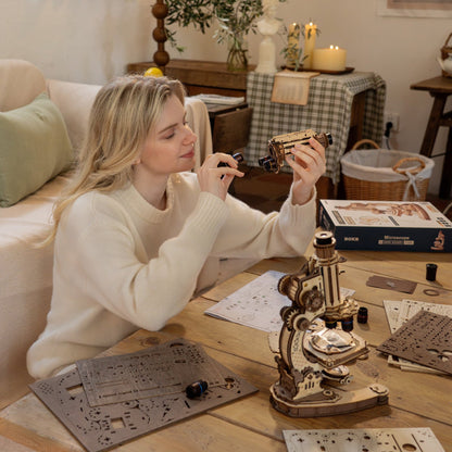 Woman working on a model kit at a table with various components and tools.