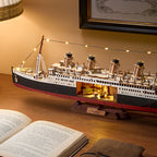 Model of a ship on a wooden surface with an open book and framed picture in the background.