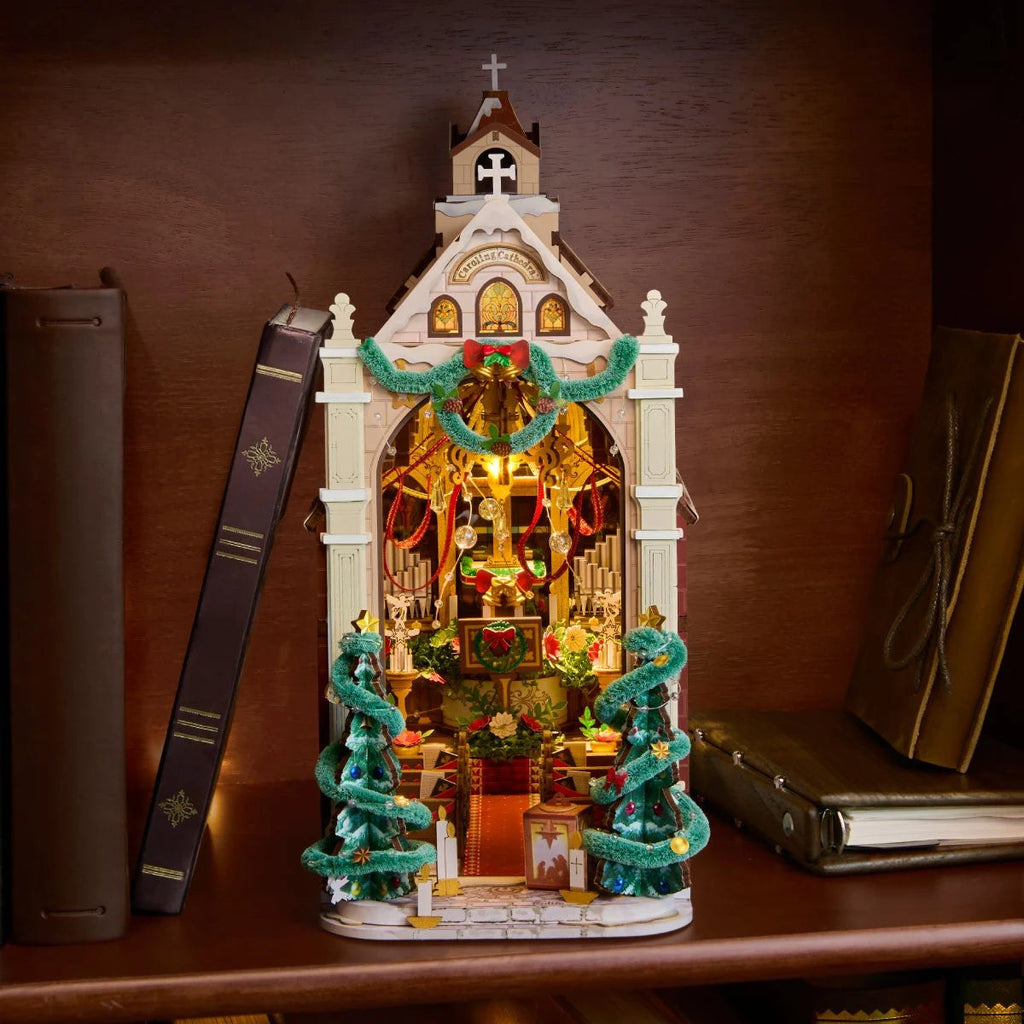 Wooden-Town Caroling Cathedral 3D wooden book nook kit – glowing cathedral on a wooden bookshelf between upright books