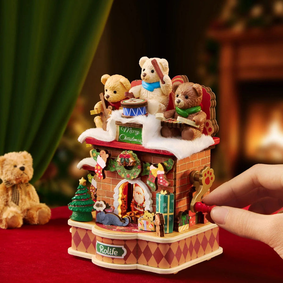 Wooden-Town Fireside Music Night 3D wooden puzzle music box – hand turning the red crank beside a plush teddy bear