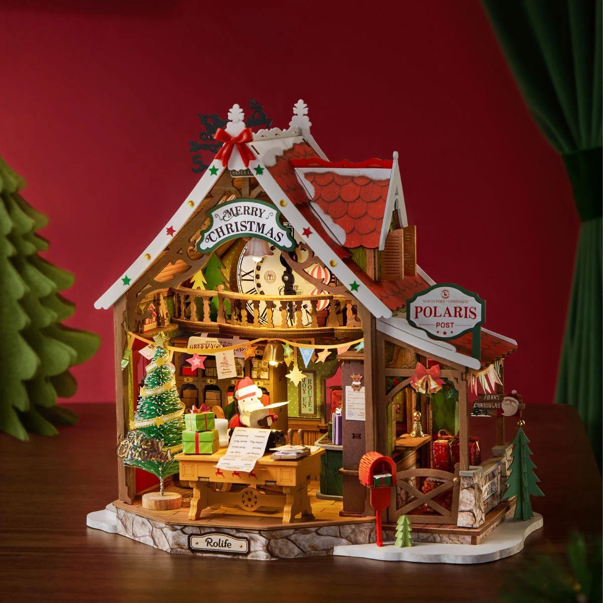 Wooden-Town Polaris Post DIY miniature house kit – post office glowing warmly against a red backdrop with a green tree