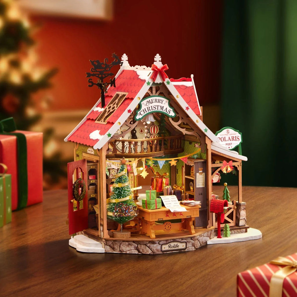 Wooden-Town Polaris Post DIY miniature house kit – open-front post office on a wooden table beside wrapped gifts