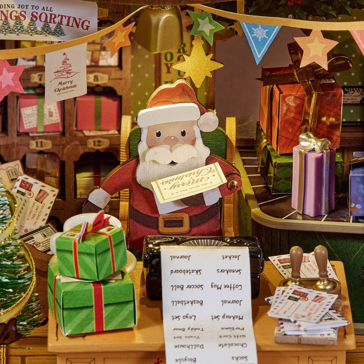 Wooden-Town Polaris Post DIY miniature house kit – close-up of Santa holding a Merry Christmas card at his desk with a list, letters and green gifts