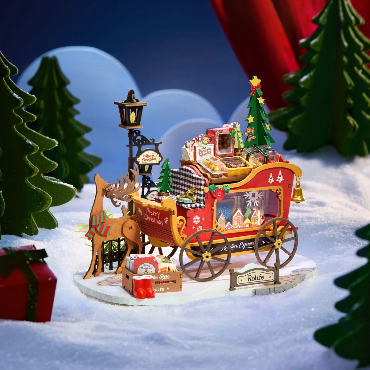 Wooden-Town Reindeer Express DIY miniature kit – sleigh scene on a snowy base against a blue backdrop with green trees